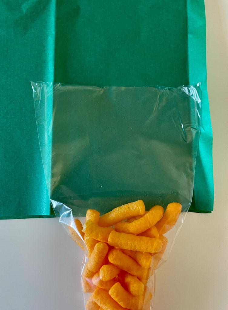 Green tissue paper, candy cone filled with cheesy chips on table