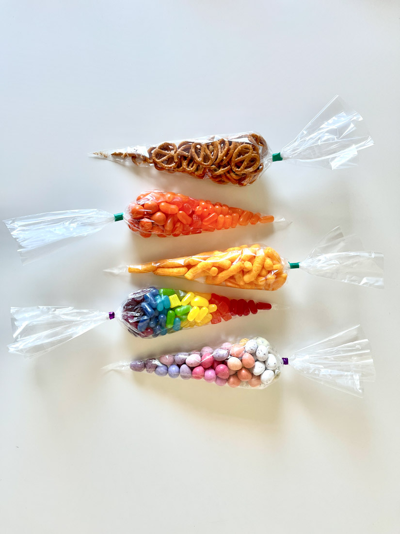 Candy Cones - four clear cone bags filled with colorful candy and pretzels on white table