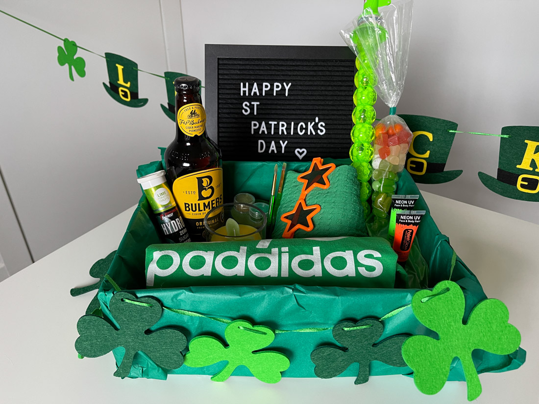 St Patrick's Day Gift Basket with green t-shirt, cider, green and orange candy on white table